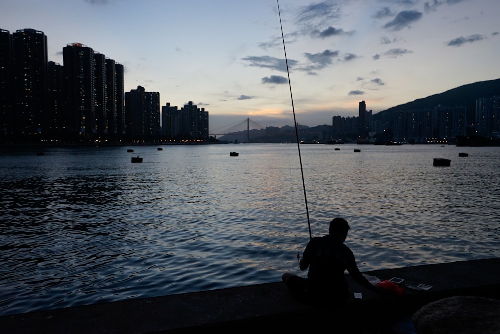 a man sitting on the edge of a body of water while fishing