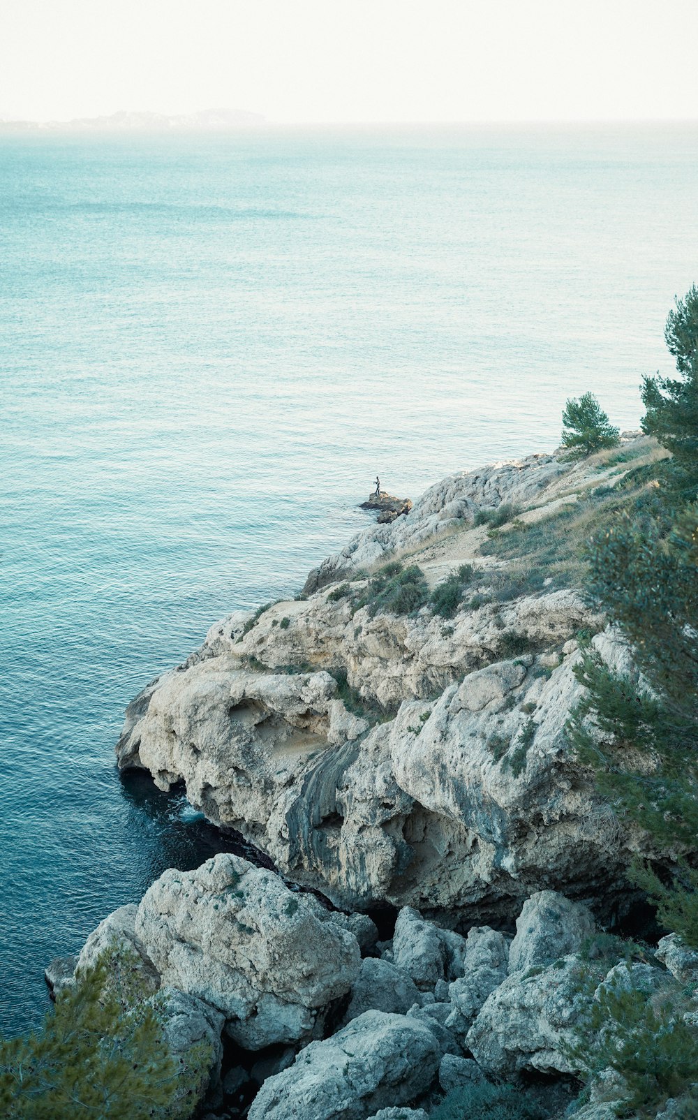 a person sitting on top of a rocky cliff next to the ocean