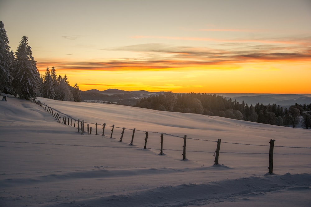 a fence in the snow with a sunset in the background