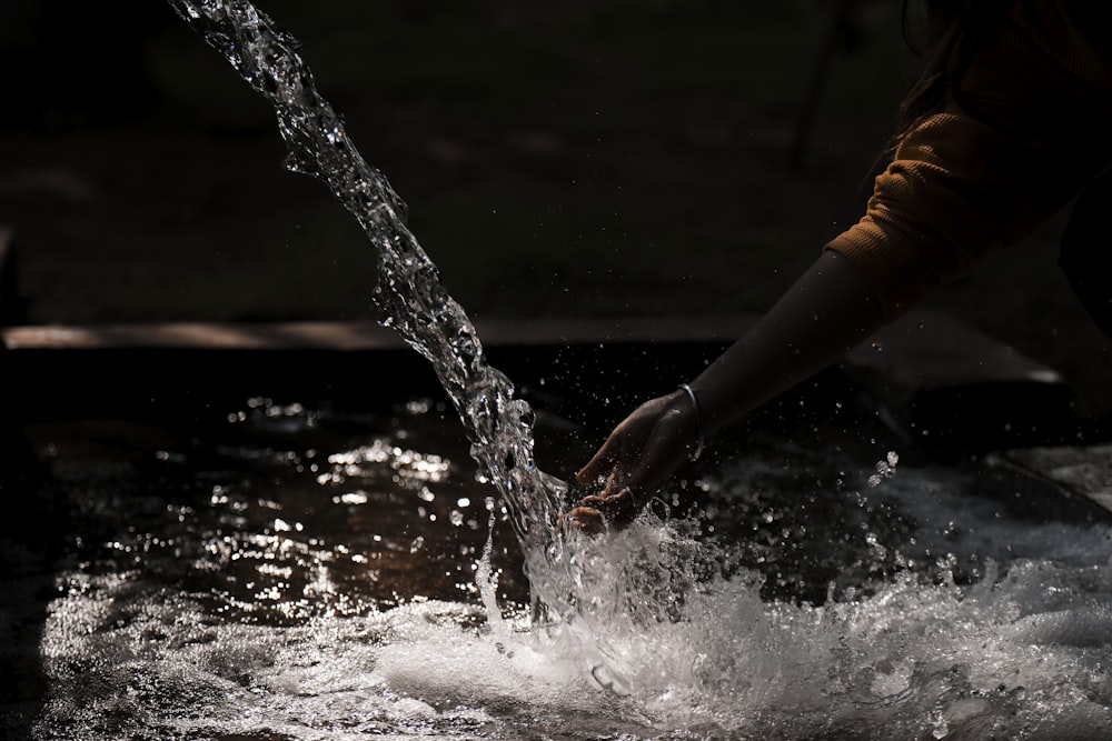 a person holding their hand out to a stream of water