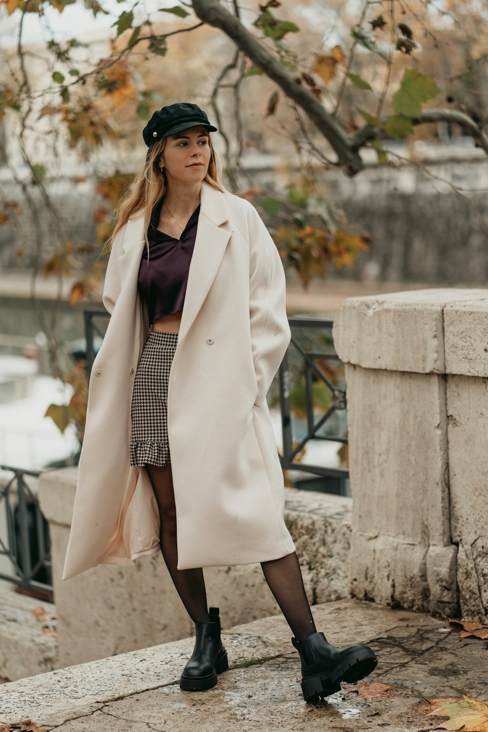 a woman in a hat and coat standing on a ledge