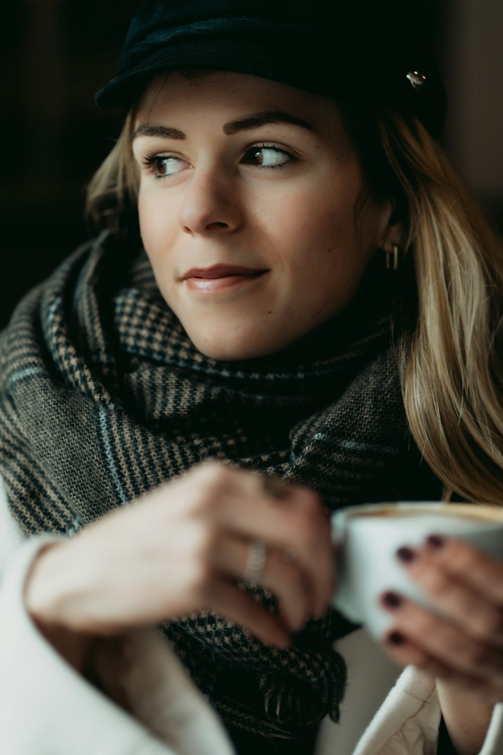 a woman wearing a hat and scarf holding a cup