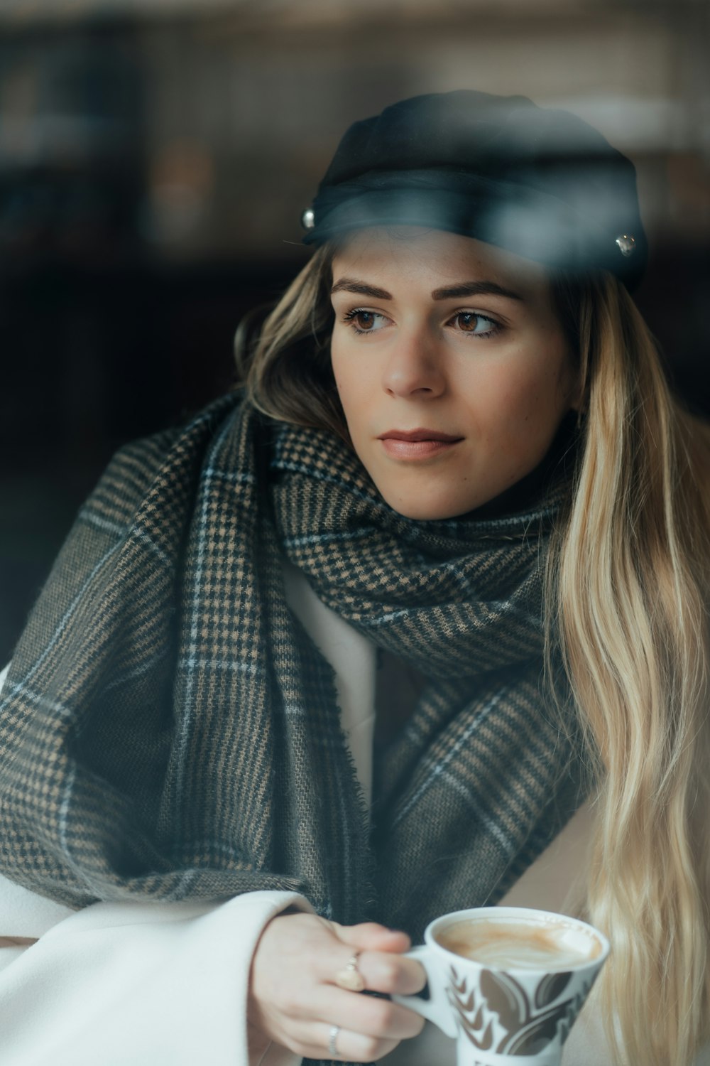 a woman wearing a hat and scarf holding a cup of coffee