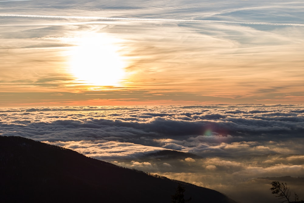 the sun is setting over the clouds in the mountains