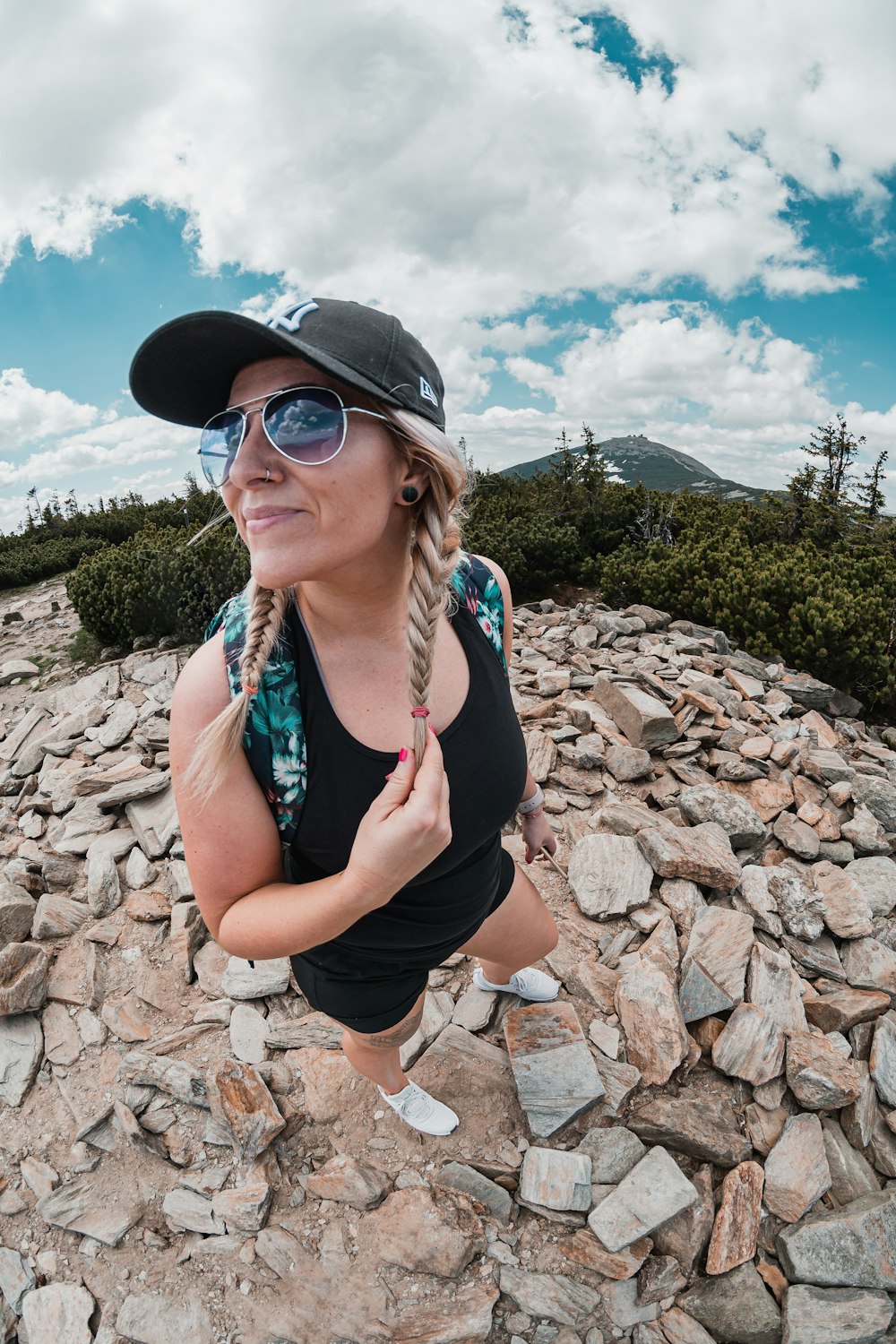 a woman in a hat and sunglasses standing on rocks