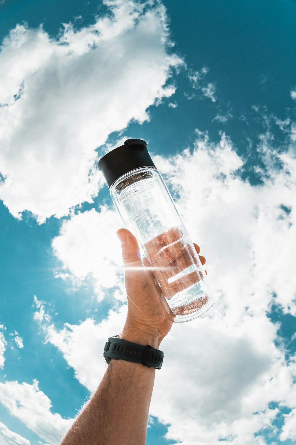 a hand holding a water bottle in front of a blue sky