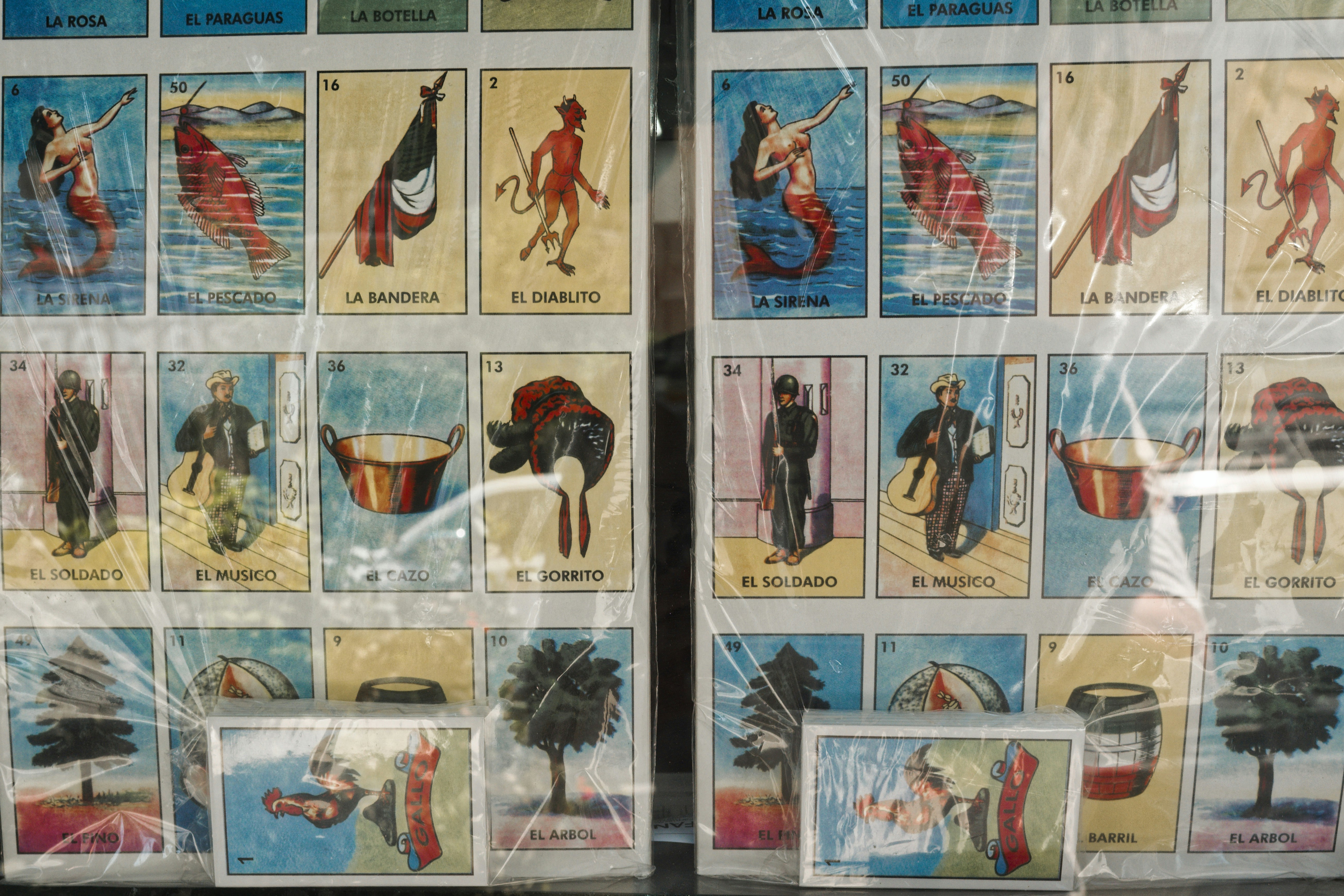 Loteria Cards Displayed in Plastic Wrap at Market Stall - A colorful display of Loteria cards is shown in a plastic-wrapped package, likely for sale at a market stall. Each card features a unique illustration and Spanish-language name.