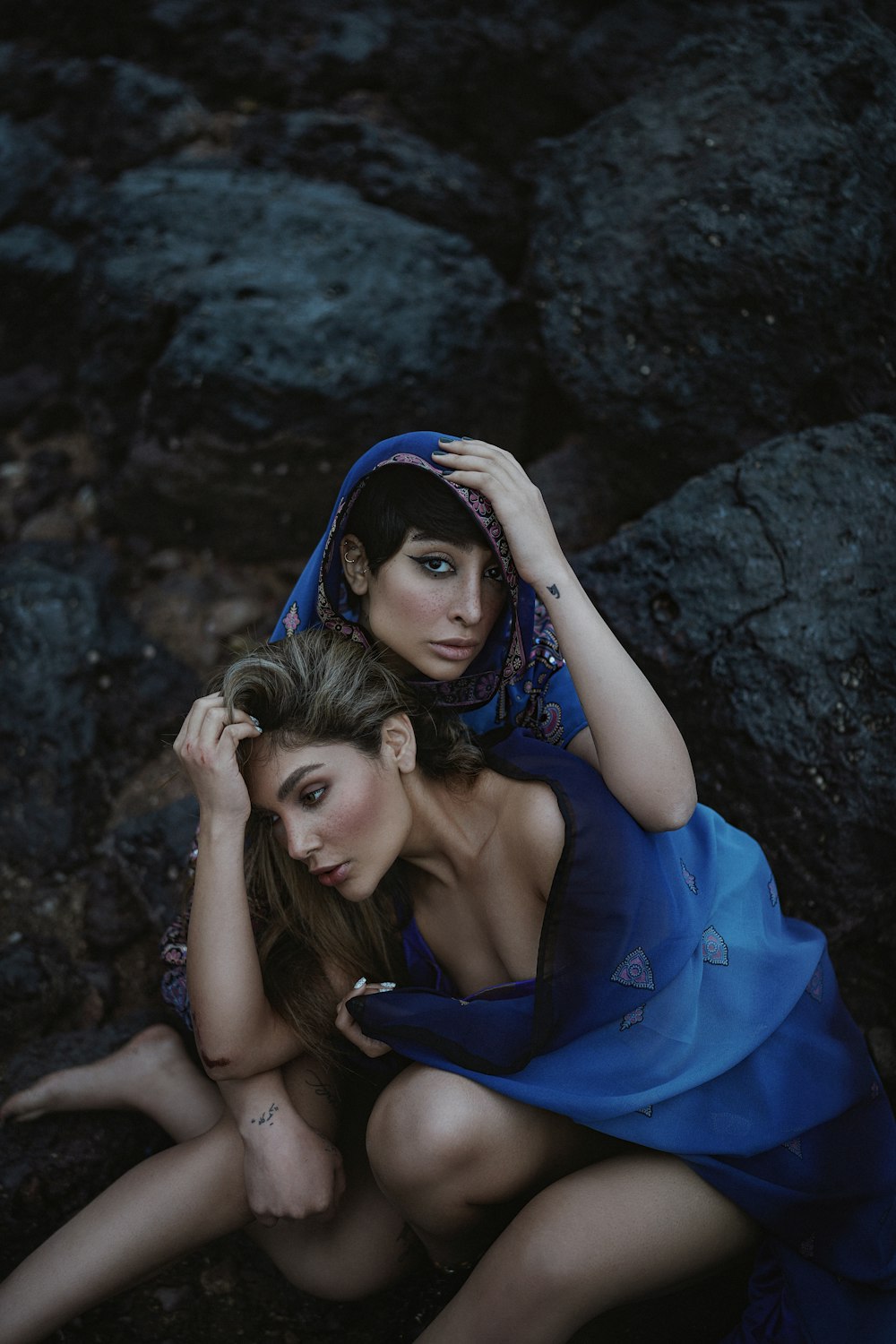 two beautiful women sitting next to each other on rocks