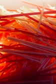 A close-up, chaotic arrangement of plastic drinking straws in various shades of red, orange, and yellow. The straws are layered and intertwined, creating a visually striking pattern with a warm, glowing light effect.