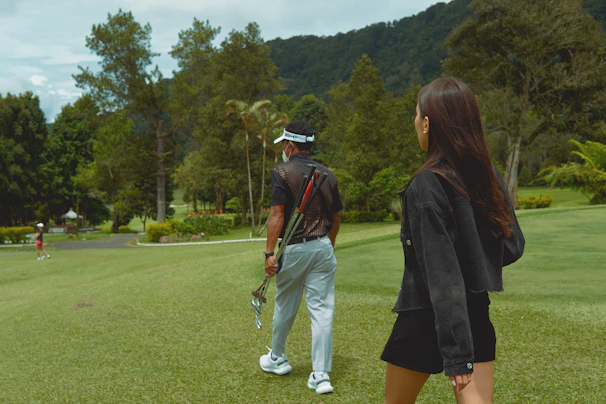 Two female friends walking side by side along a lush green fairway, golf bags slung over their shoulders.
