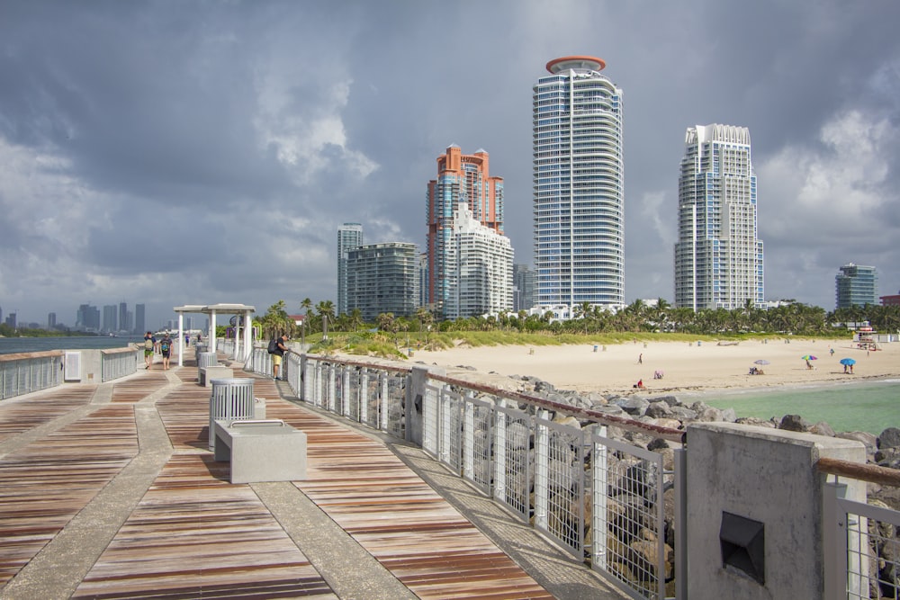 a wooden walkway leading to a beach with tall buildings in the background