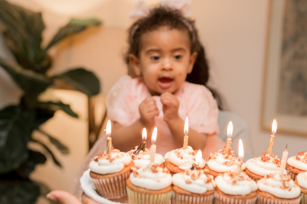 a little girl sitting in front of a plate of cupcakes