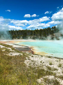 A serene hot spring surrounded by lush green mountains under a clear blue sky.