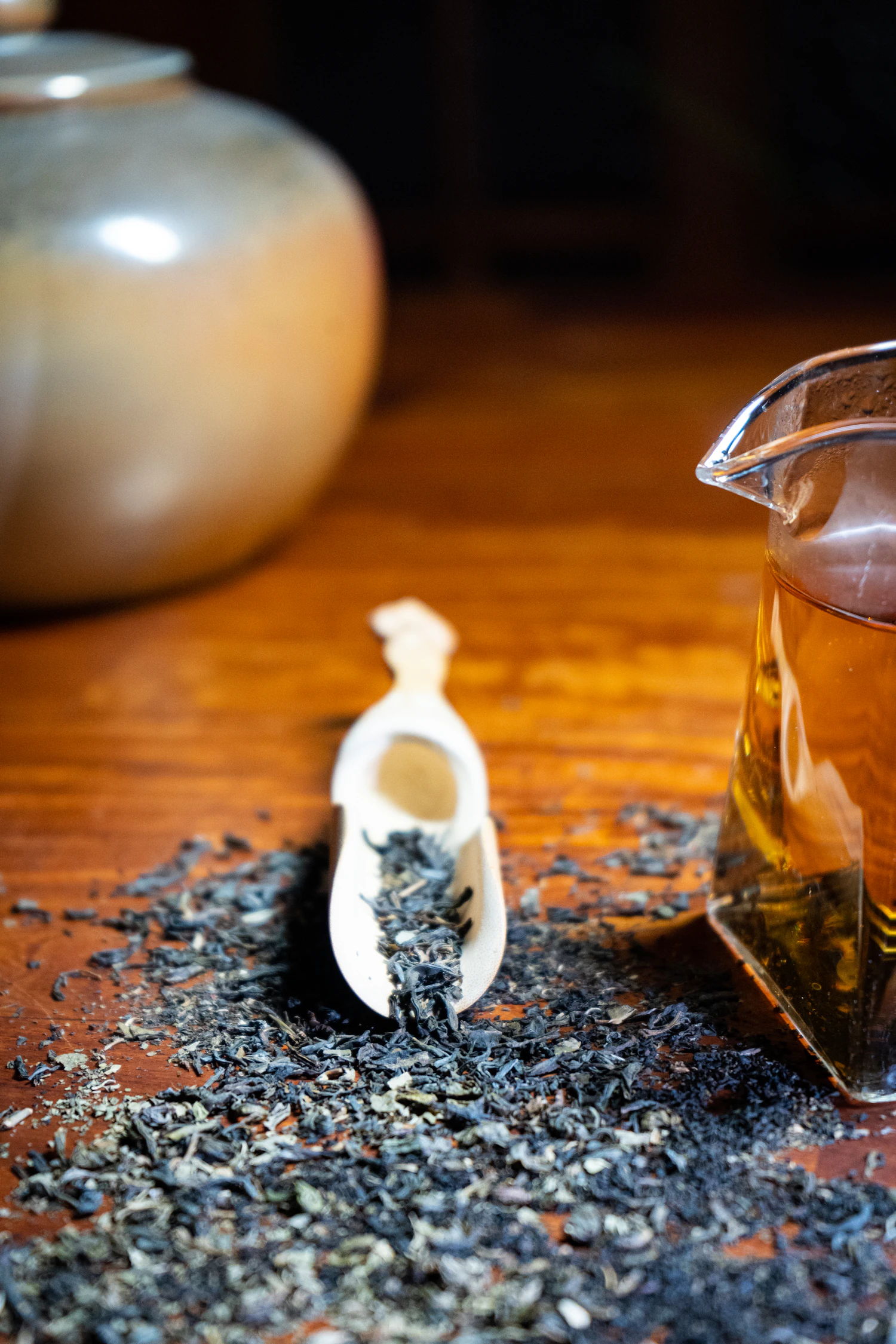Dark green Anxi Iron Bell leaf spilled across the table beside its gaiwan, in stock