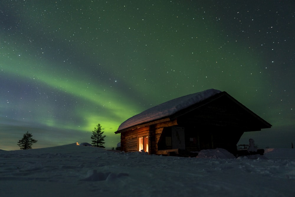 a cabin in the snow under a green aurora bore