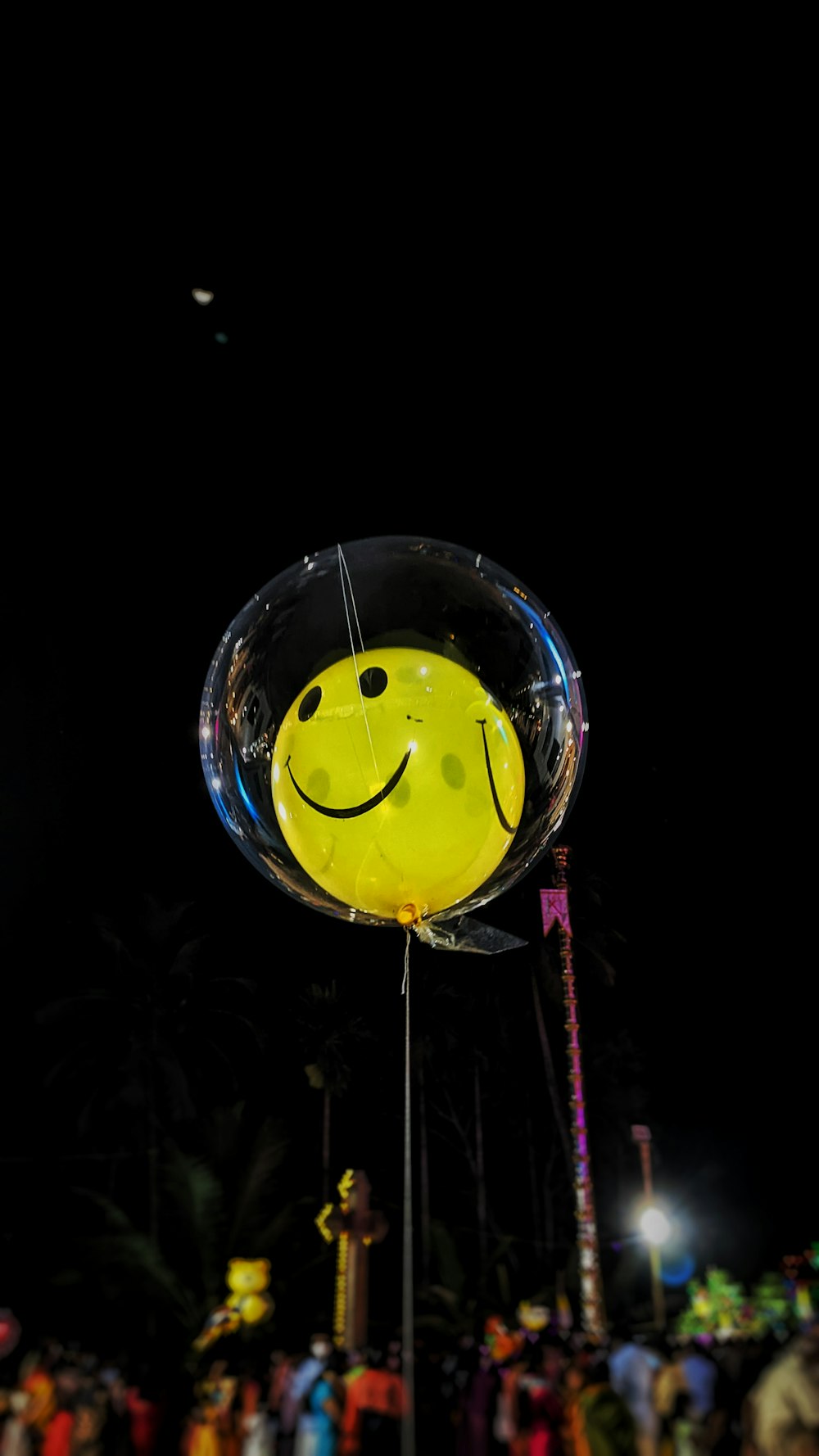 a yellow smiley face balloon sitting on top of a pole