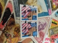 A collection of colorful postage stamps overlapping each other. In the center, there are two US stamps featuring the American flag and a building. Surrounding them are various international stamps with different designs and portraits.
