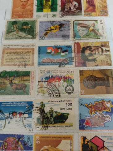The image features a collection of various Indian postage stamps, each with unique designs and themes. The stamps depict a range of subjects including historical figures, animals, national symbols, and significant events. The stamps come in different colors and denominations, and some are marked with postal cancellation marks.