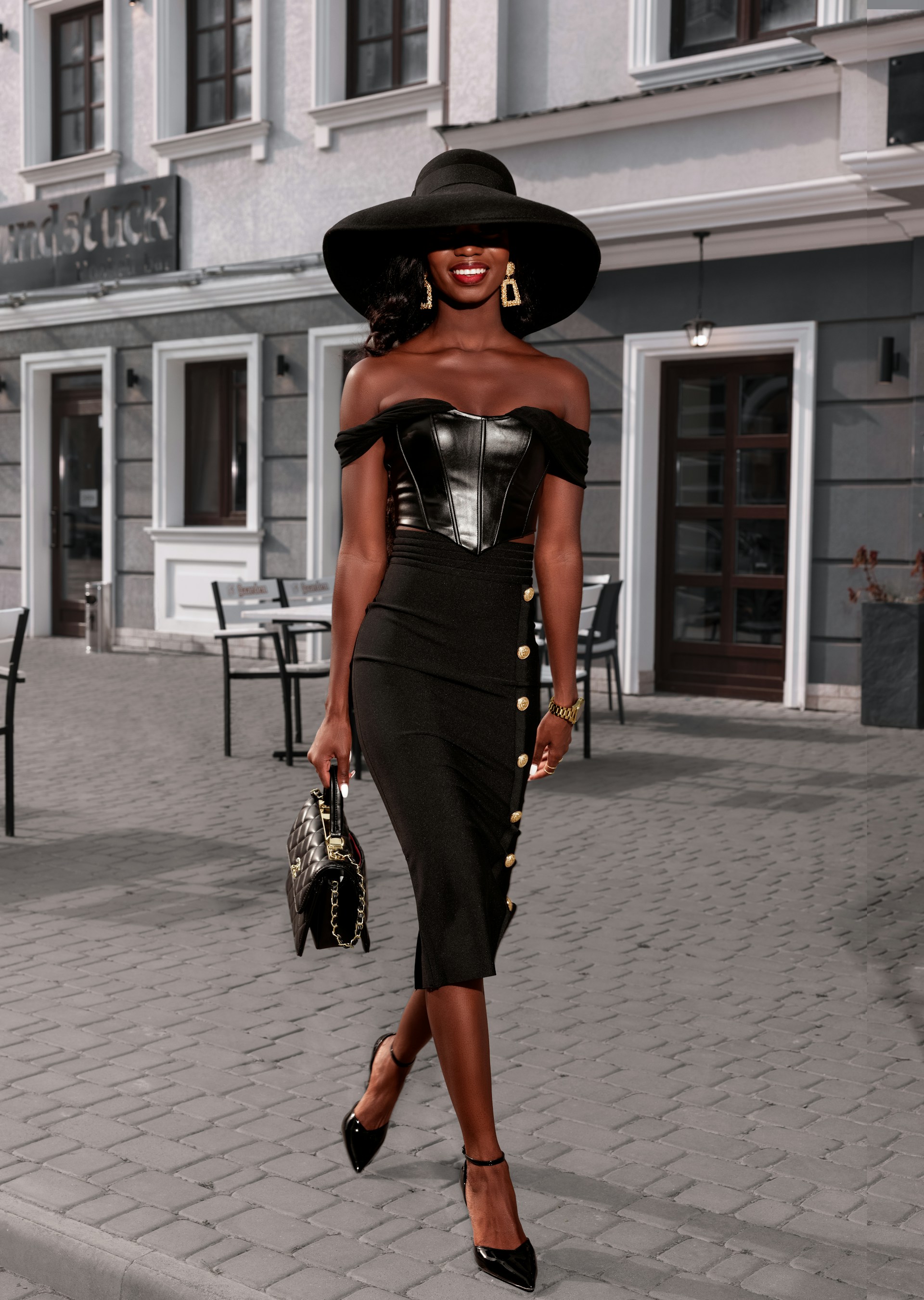 a woman in a black dress and hat walking down a street