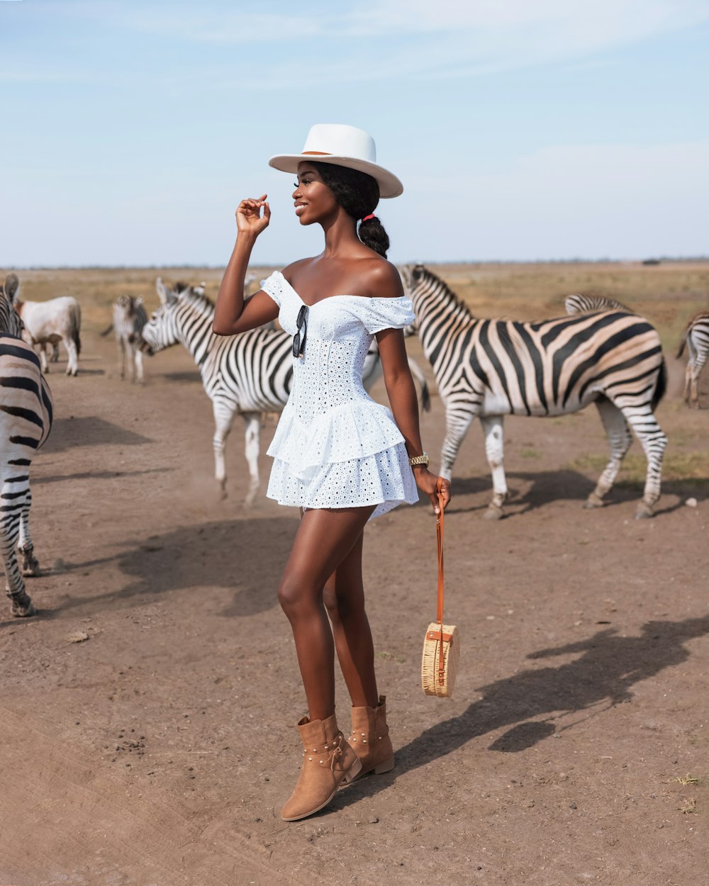 a woman in a white dress and hat standing in front of zebras