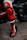 A close-up of a person wearing black and red motorcycle racing gear with branding visible, standing next to a sleek black motorcycle on cobblestone pavement.