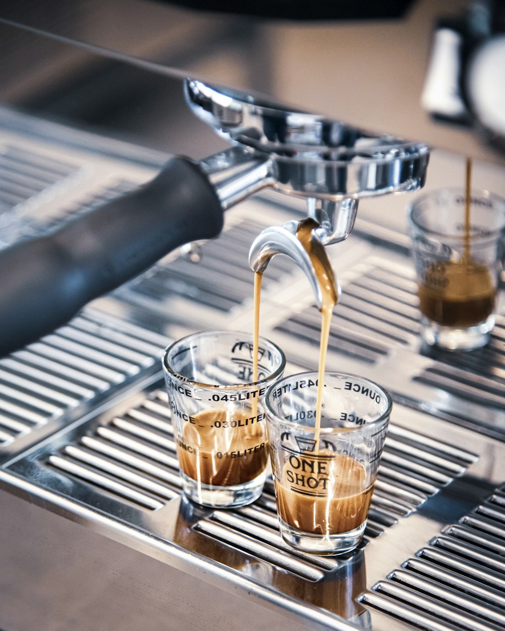 two shot glasses filled with coffee being poured into a espresso machine