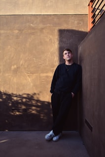 a man leaning against a wall with his hands on his hips