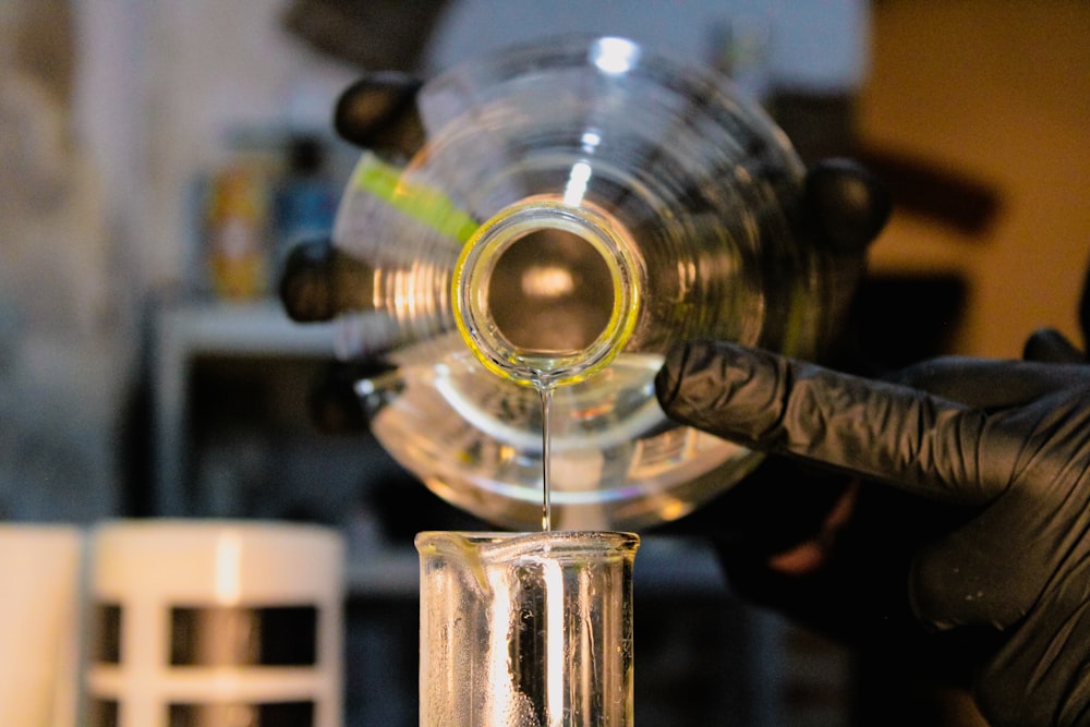 a person in a black glove is pouring liquid into a test tube