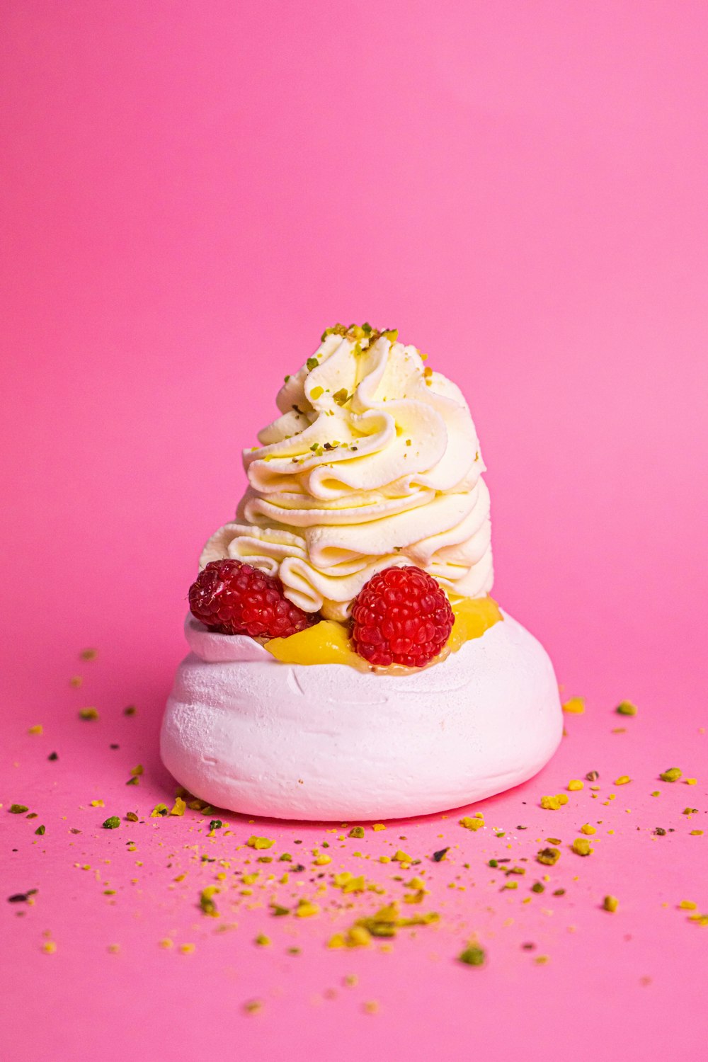 a dessert with whipped cream and raspberries on a pink background