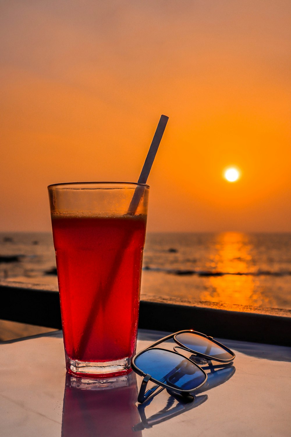 una bebida y gafas de sol en una mesa cerca del océano