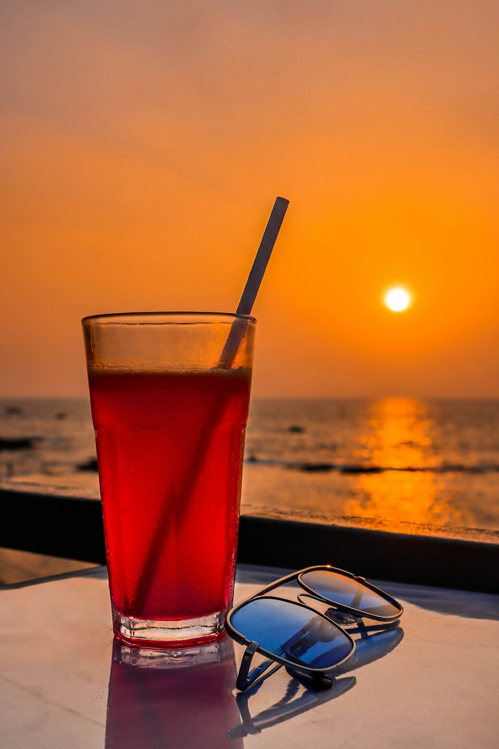 a drink and sunglasses on a table near the ocean