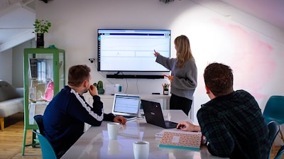 A consultant presenting data on a large screen to attentive clients in a bright office.