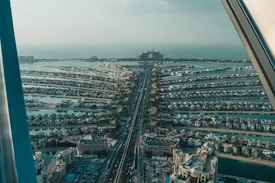 An aerial view of a man-made archipelago with numerous residential villas arranged in a distinct pattern resembling a palm tree. A long, straight road runs down the center, leading towards a large, iconic hotel in the distance. The sea surrounds the intricately designed islands.