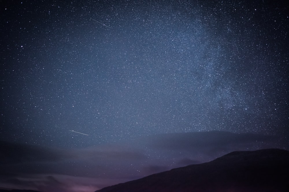 the night sky with stars above a mountain