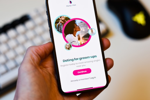 A hand holds a smartphone displaying a dating app interface. The screen shows profiles of adults with a text 'Dating for grown-ups' encouraging registration to connect with singles nearby. Profiles are highlighted with circular images.