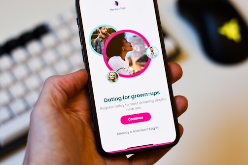 A hand holds a smartphone displaying a dating app interface. The screen shows profiles of adults with a text 'Dating for grown-ups' encouraging registration to connect with singles nearby. Profiles are highlighted with circular images.