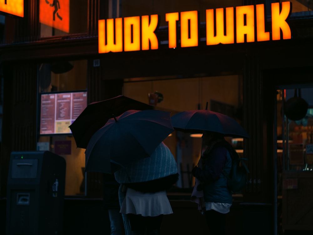Ein paar Leute stehen unter Regenschirmen vor einem Gebäude