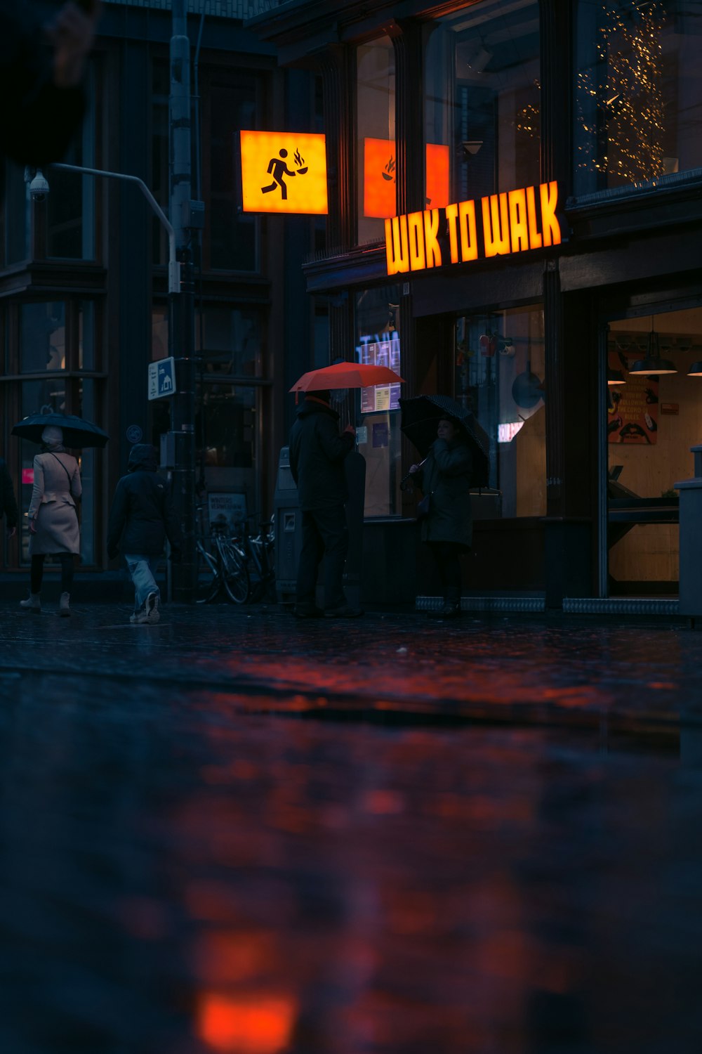 Una calle de la ciudad por la noche con gente sosteniendo paraguas