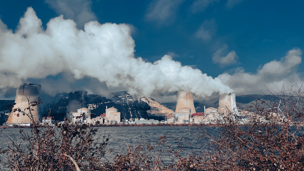 smoke billows from a factory near a body of water