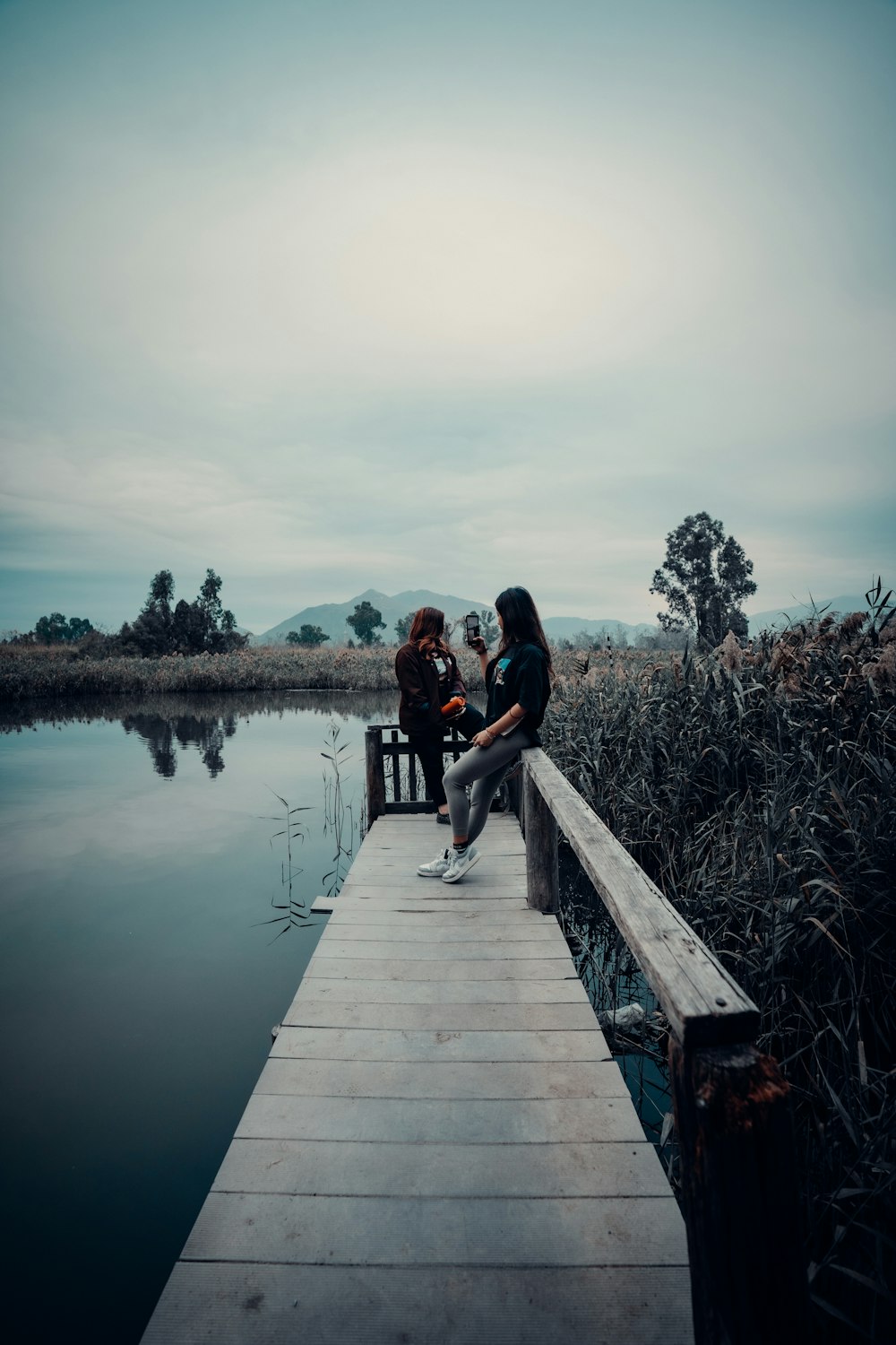 two people sitting on a dock next to a body of water