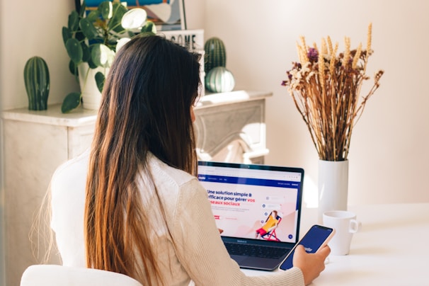 Une femme qui travail sur un ordinateur et un téléphone et qui navigue sur le site web Booking.com