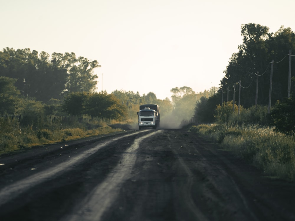 a truck driving down a dirt road next to a forest