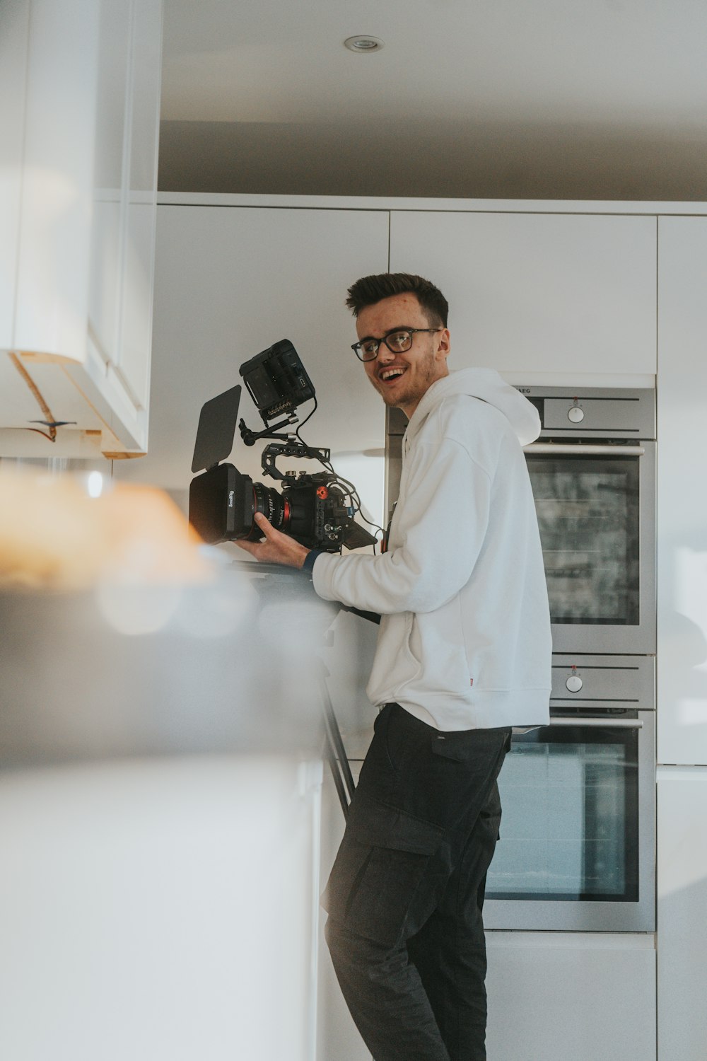 Ein Mann steht in einer Küche und hält eine Kamera in der Hand