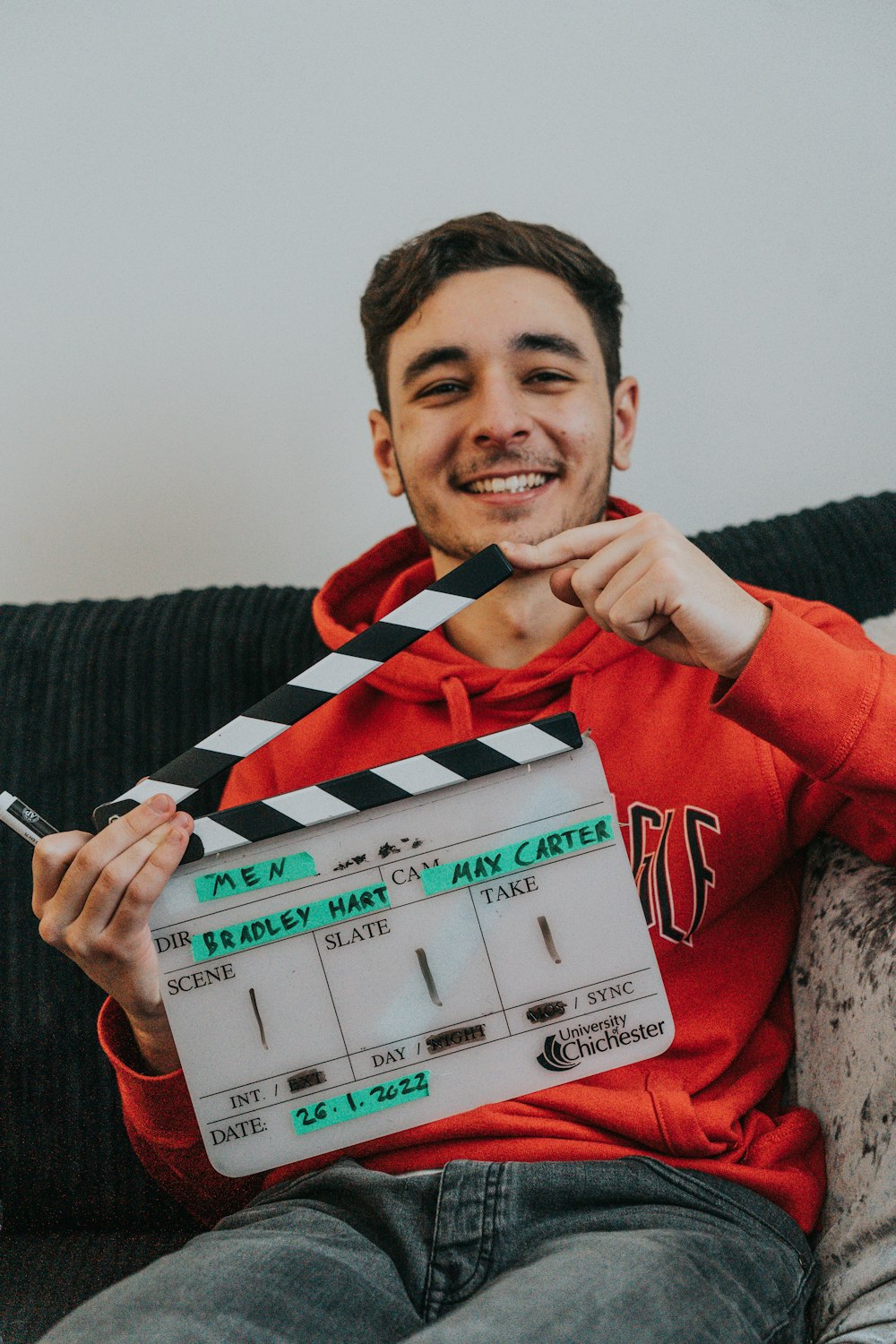 a man sitting on a couch holding a movie clapper