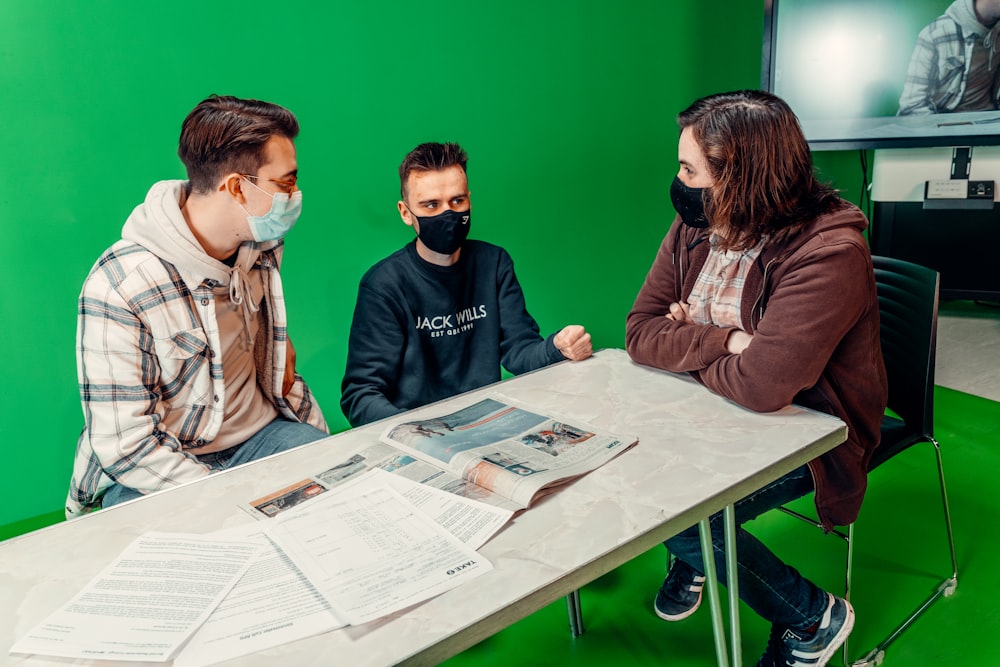 three people sitting at a table in front of a green screen
