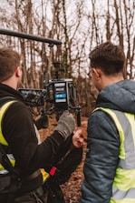 two men in vests standing in front of a camera