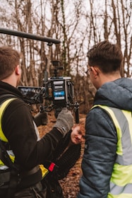 two men in vests standing in front of a camera