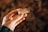 A hand holding a wine cork with the word 'Kutman' printed on it, against a blurred background. The cork appears slightly worn, suggesting it might have been used. The hand is well-manicured, with light-colored polish on the nails.