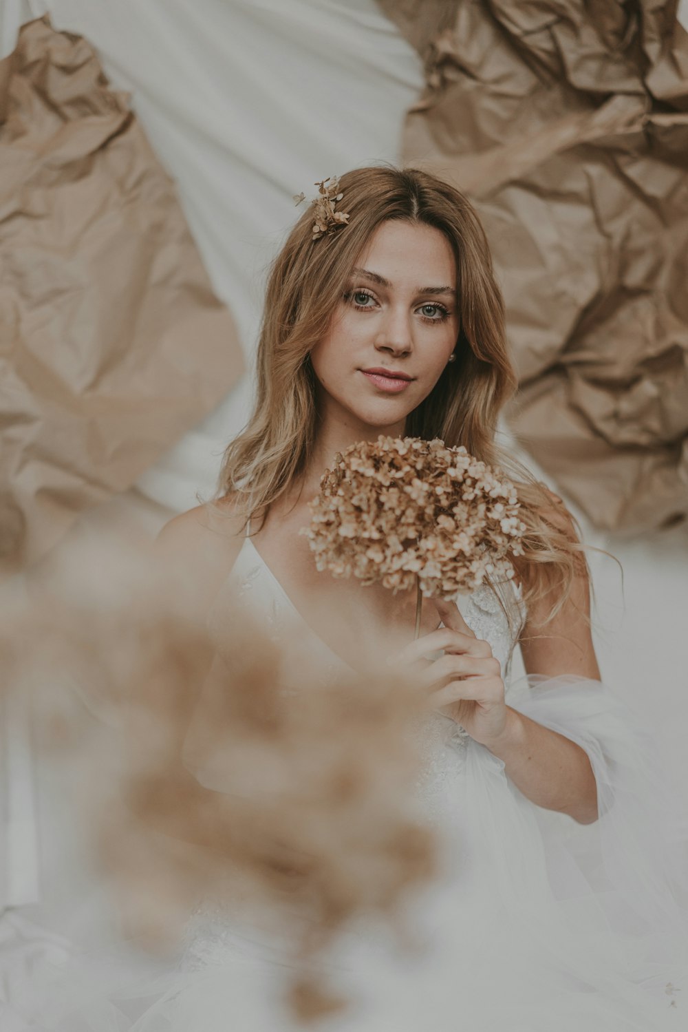 a woman in a white dress holding a bouquet of dried flowers