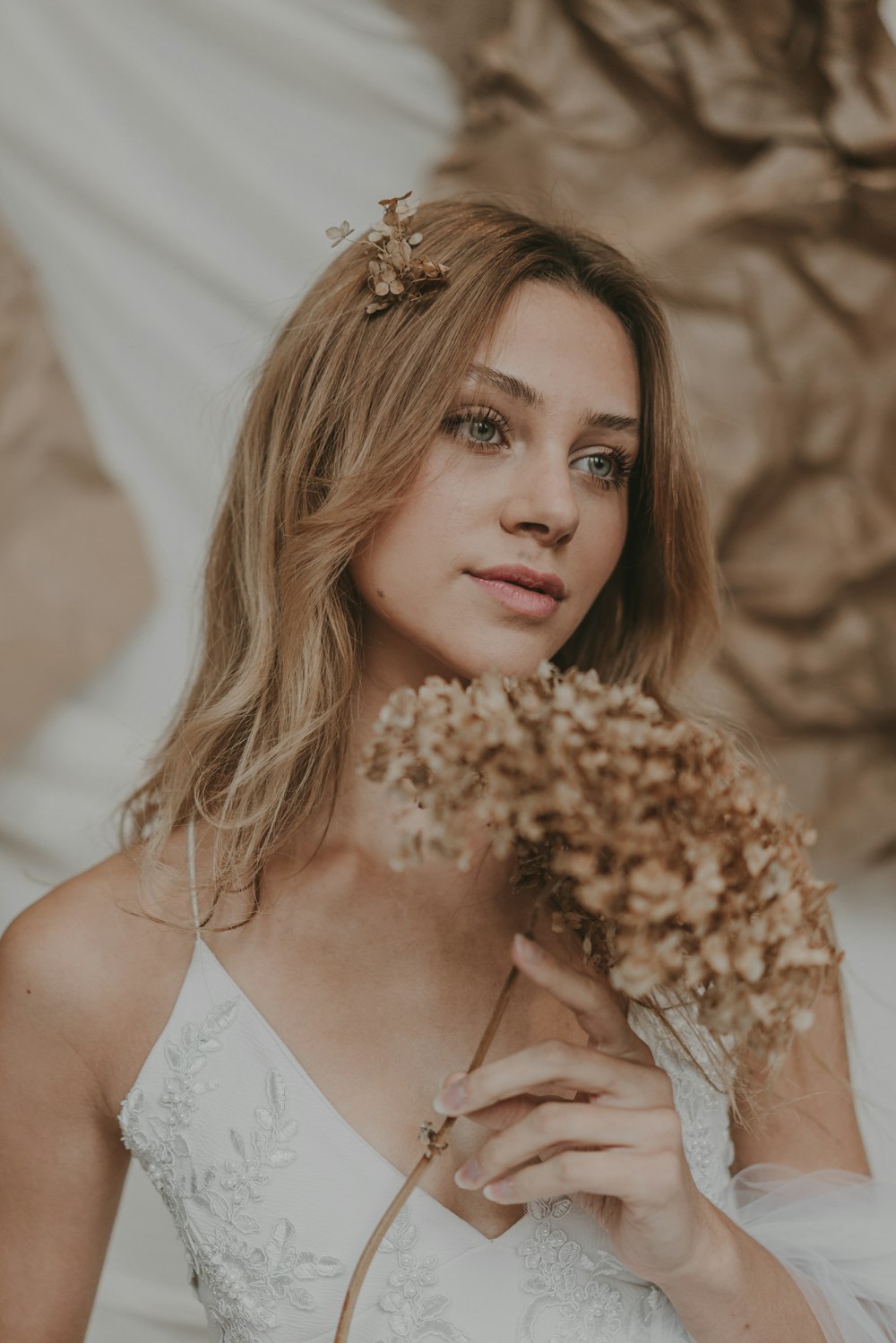 a woman in a white dress holding dried flowers